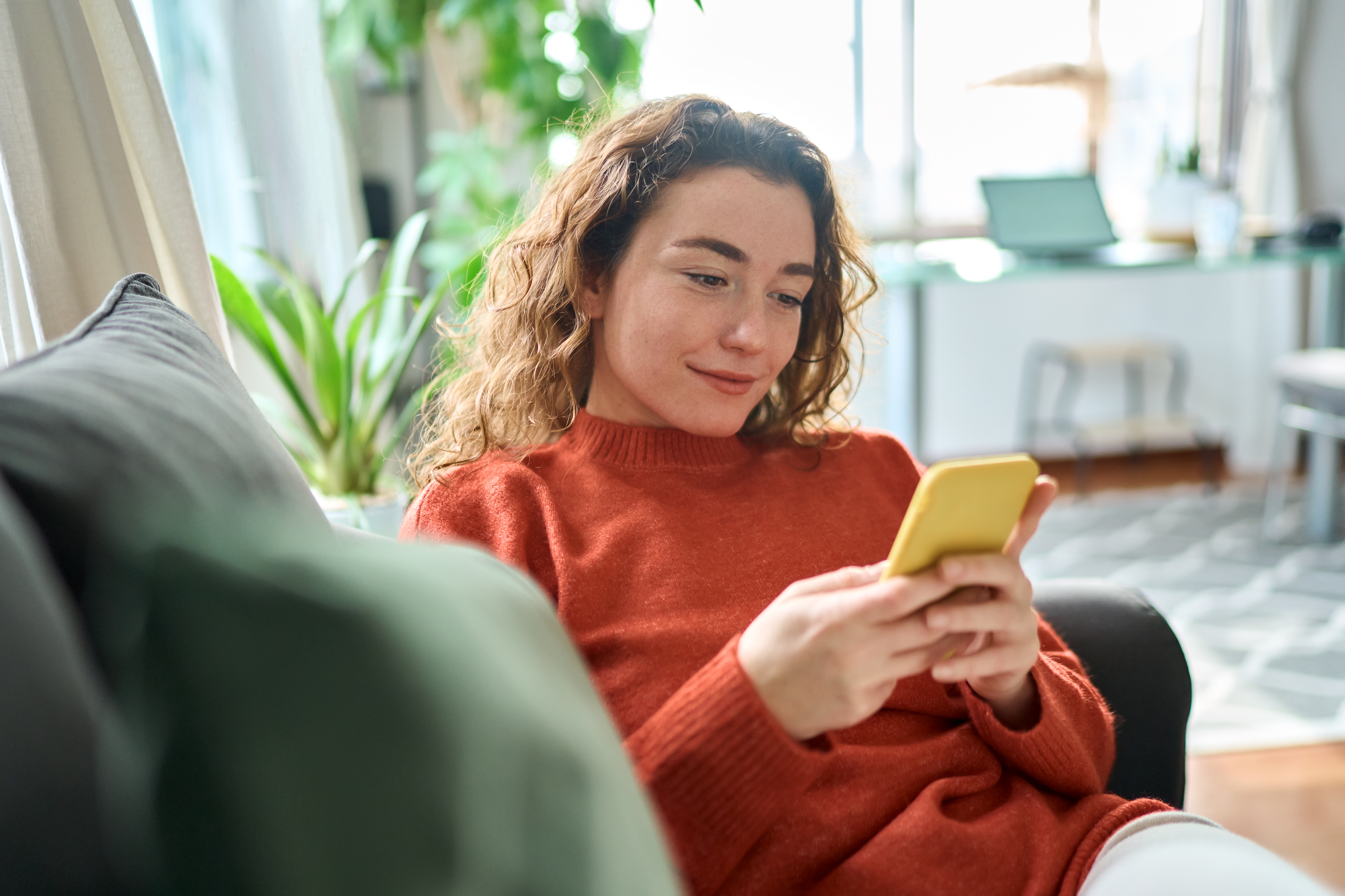Smiling relaxed young woman sitting on couch using mobile phone technology..jpeg